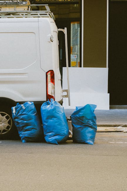 The image shows the rear part of a white commercial van parked on an urban street, with three large blue rubbish bags placed on the ground directly behind the vehicle. The bags appear to be filled wit